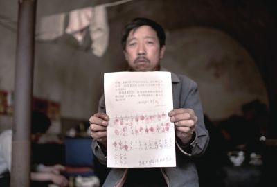 村民举着一张按有26个红手印和写着36个签名的申诉书。